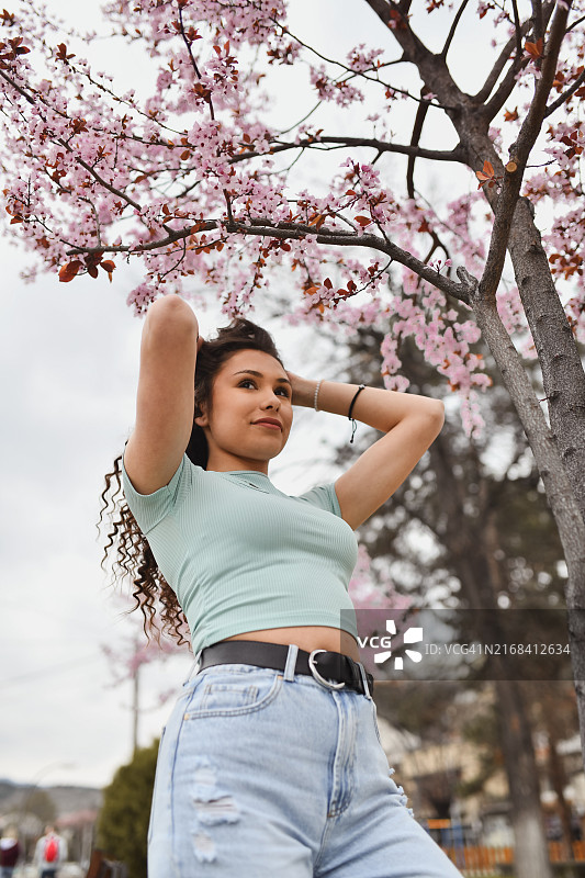 粉色树旁拨弄卷发的女人图片素材