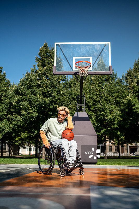 在阳光明媚的公园球场上独自一人坐在轮椅上拿着篮球的残疾男子图片素材