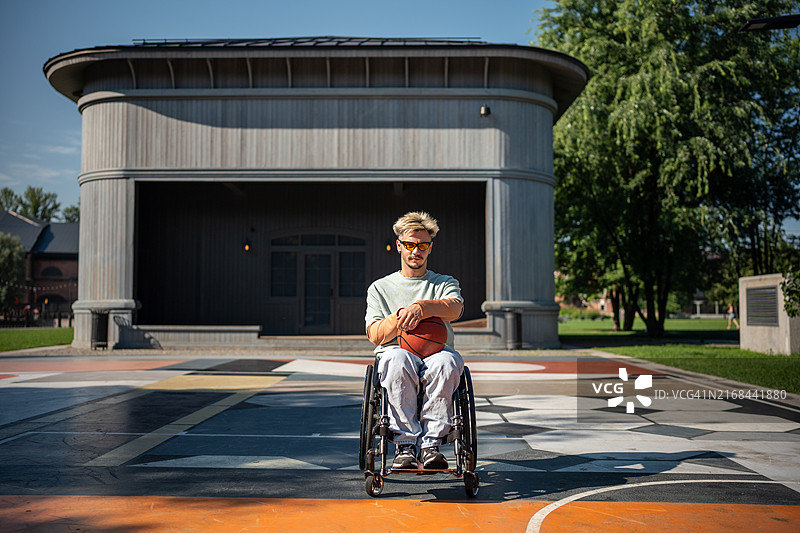 在阳光明媚的公园球场上独自一人坐在轮椅上拿着篮球的残疾男子图片素材