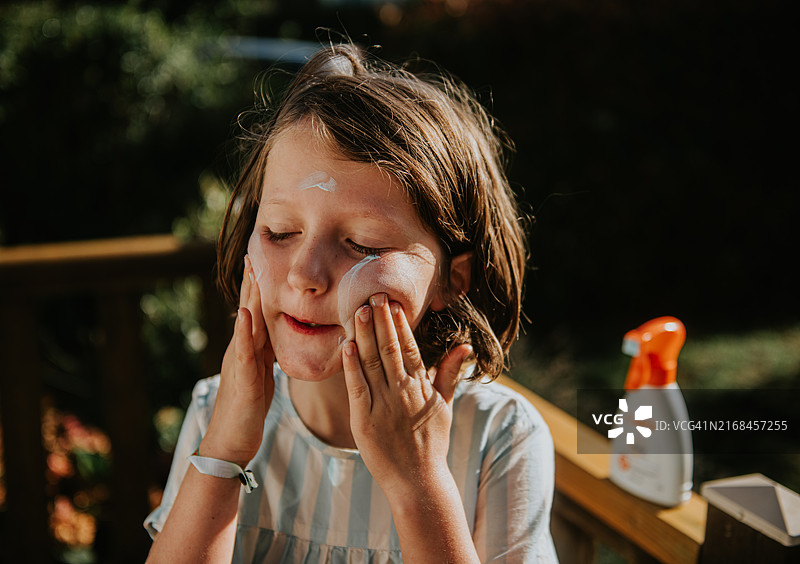 小孩在后院仔细地在脸颊上涂抹防晒霜图片素材