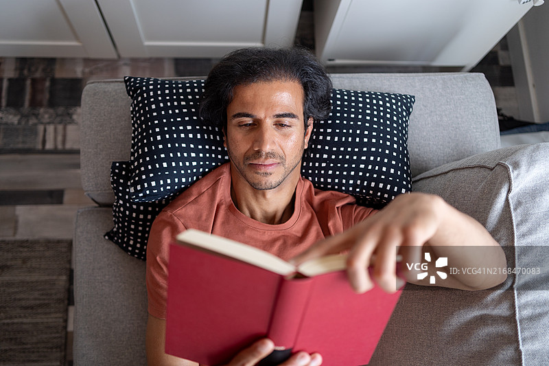 年轻男人斜倚在沙发上，沉浸在迷人的书中，享受宁静的时刻图片素材
