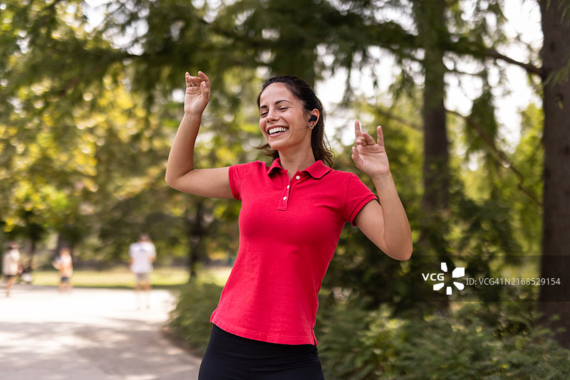 快乐的女人在公园里穿着红色 polo 衫跳舞图片素材