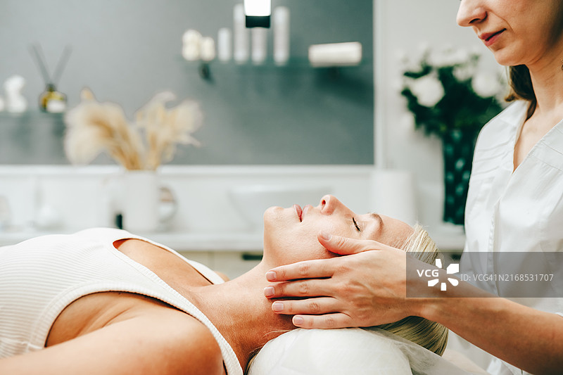 面部水疗护理：放松的女人在诊所接受淋巴引流面部按摩图片素材