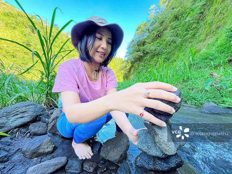 年轻女人在鹅卵石河边堆叠平衡石图片素材
