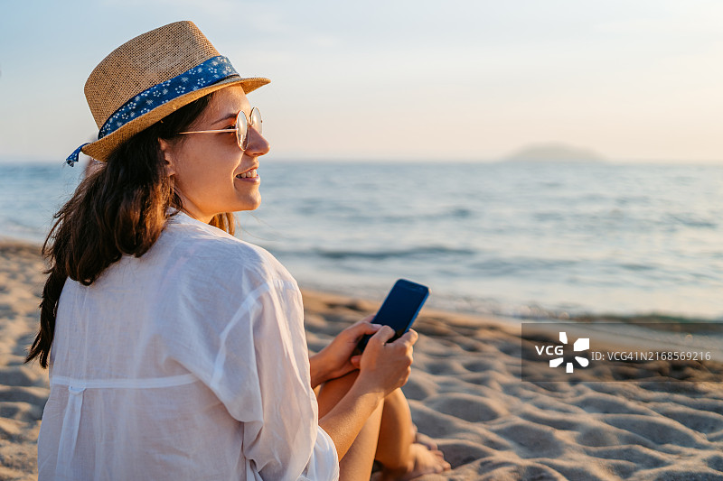 年轻女人在尼奥斯·马尔马拉斯海滩日落时使用手机图片素材