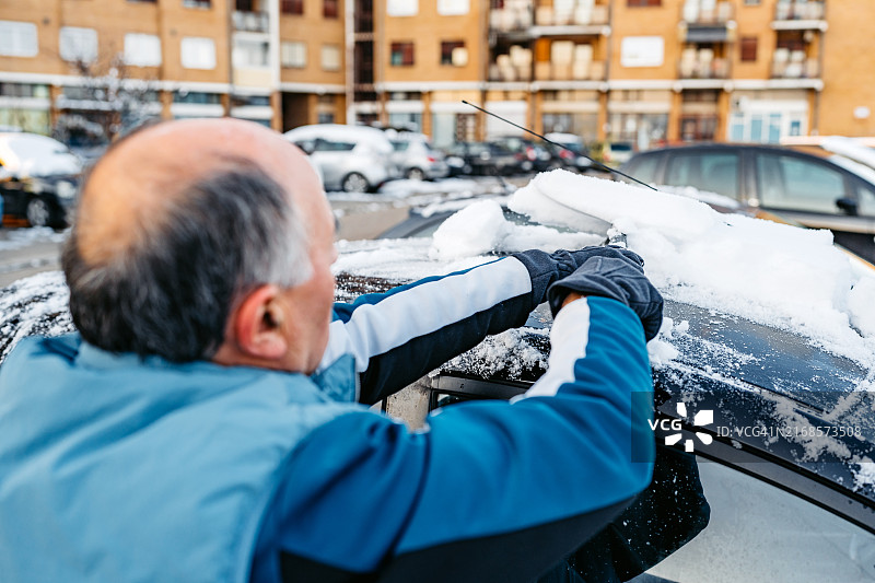 老年男人在停车场清理汽车上的积雪图片素材
