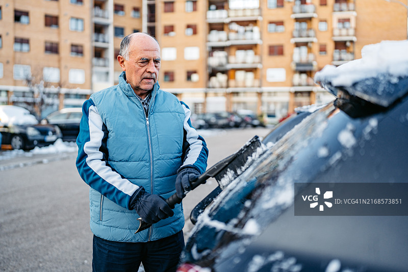 老年男人在停车场清理汽车上的积雪图片素材