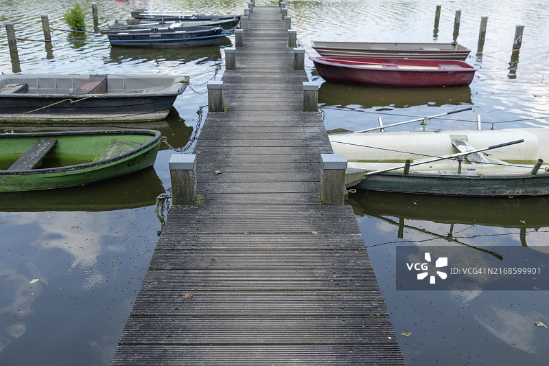 通往漂浮在平静水面上的几艘船的木制码头，位于德国北莱茵-威斯特法伦州博尔肯图片素材