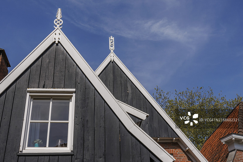 两座房屋：白色烟囱、深灰色木制外墙和窗户，位于荷兰奥特马瑟姆的蓝天和树木前图片素材