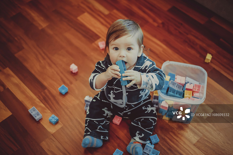 穿着睡衣的宝宝坐在木地板上玩彩色积木图片素材