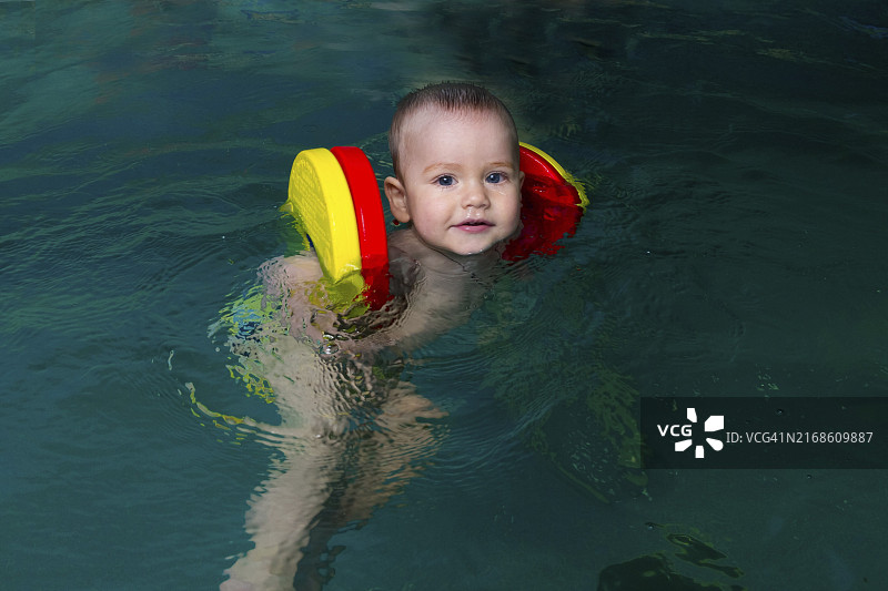 戴着彩色游泳圈在泳池里游泳的婴儿，享受游泳乐趣，充满安全感和快乐图片素材