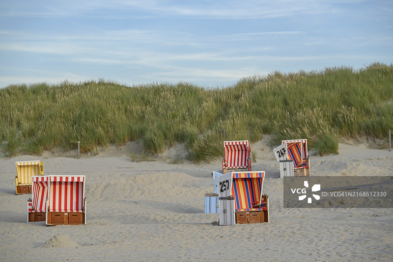 安静的沙滩上散落着色彩缤纷的沙滩椅，位于德国东弗里西亚Langeoog的绿色沙丘前图片素材