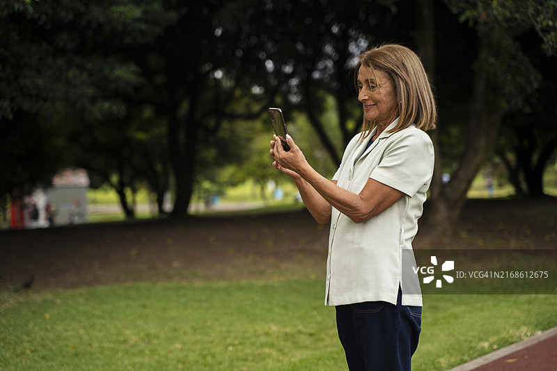 走在公园里，一边看手机一边拍照的中年妇女图片素材