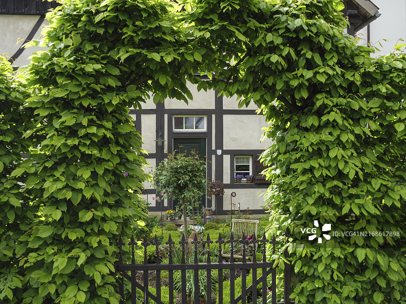 德国北莱茵-威斯特法伦州赫滕市的绿色房屋入口，拱门由树叶、花园和乡村栅栏构成图片素材