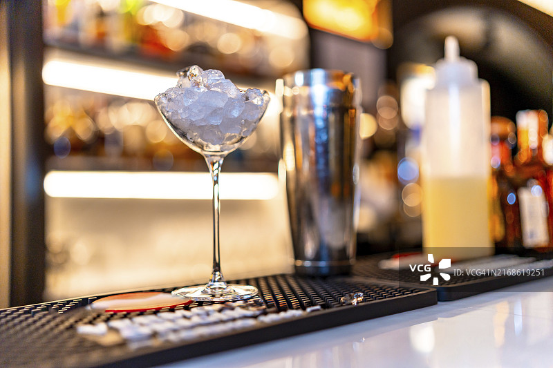 夜间酒吧柜台上鸡尾酒调酒器旁边的冰镇马提尼酒杯图片素材