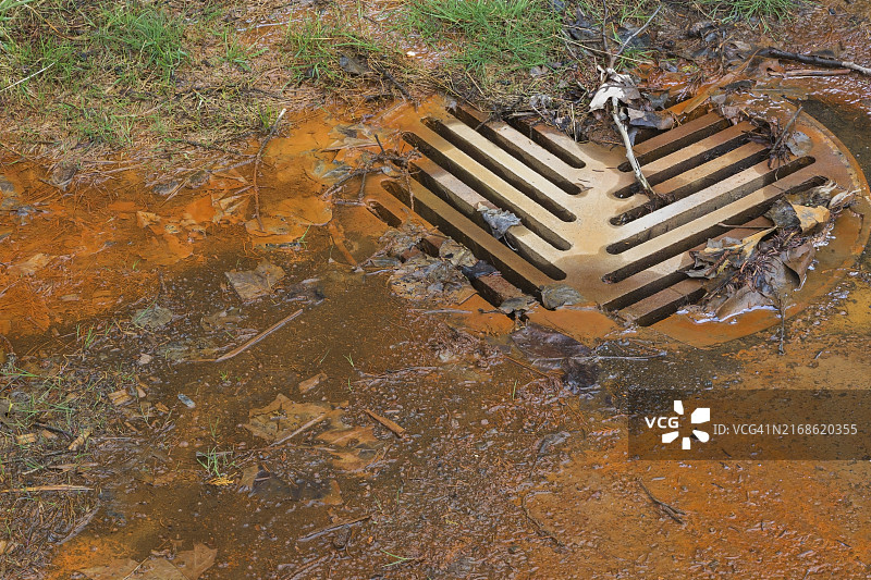 受污染的铁锈色水流入春季草坪边缘的下水道系统，加拿大魁北克，北美图片素材