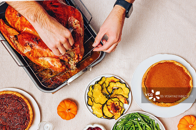 感恩节餐桌上，一人正在雕刻金棕色的烤火鸡，桌上摆满了包括青豆、南瓜、蔓越莓酱和南瓜派在内的传统菜肴，都柏林，加利福尼亚州，美国图片素材