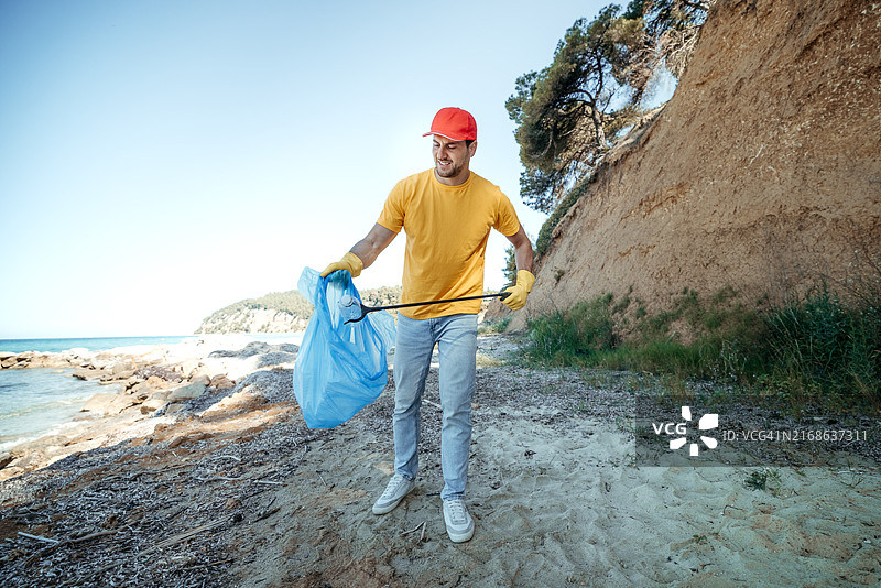 身穿黄色衬衫和红色帽子的青年志愿者清理海滩图片素材