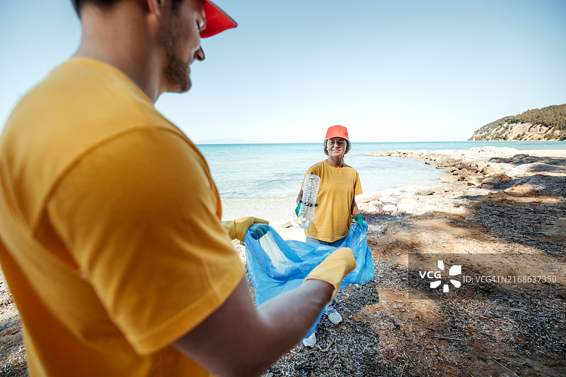 年轻夫妇穿着制服在阳光明媚的海滩上一起清洁图片素材
