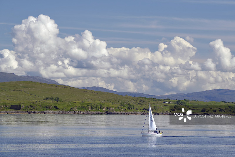 苏格兰奥班穆尔岛，多云天空下，广阔的大自然和群山环绕的平静水面上的一叶孤帆图片素材