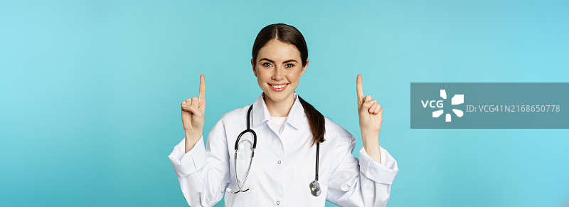 自信的年轻女医生肖像，身穿白大褂，手指向上微笑图片素材