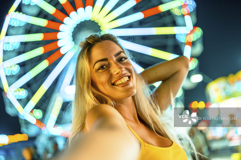 游乐园里自拍的快乐美女的个人视角（背景是霓虹灯照亮下的摩天轮）图片素材