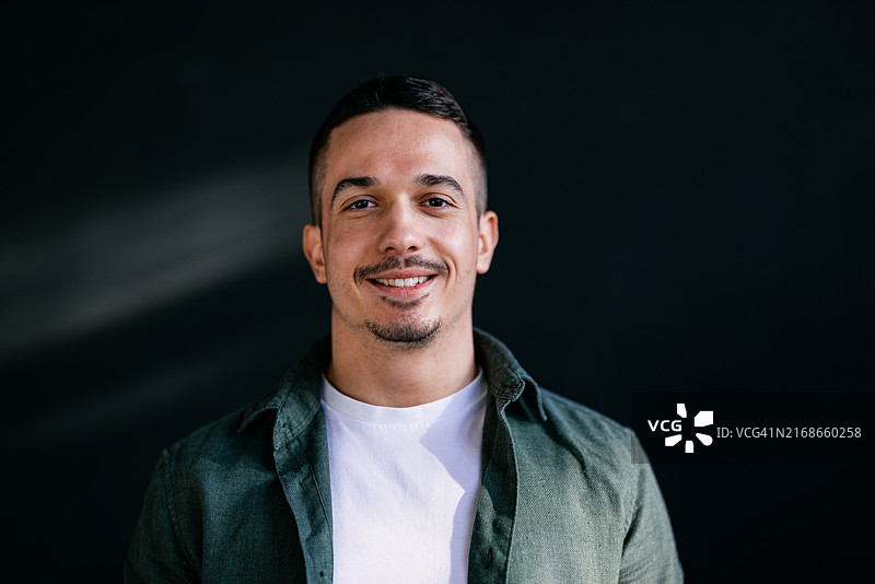 自信的年轻男子在深色背景前微笑图片素材
