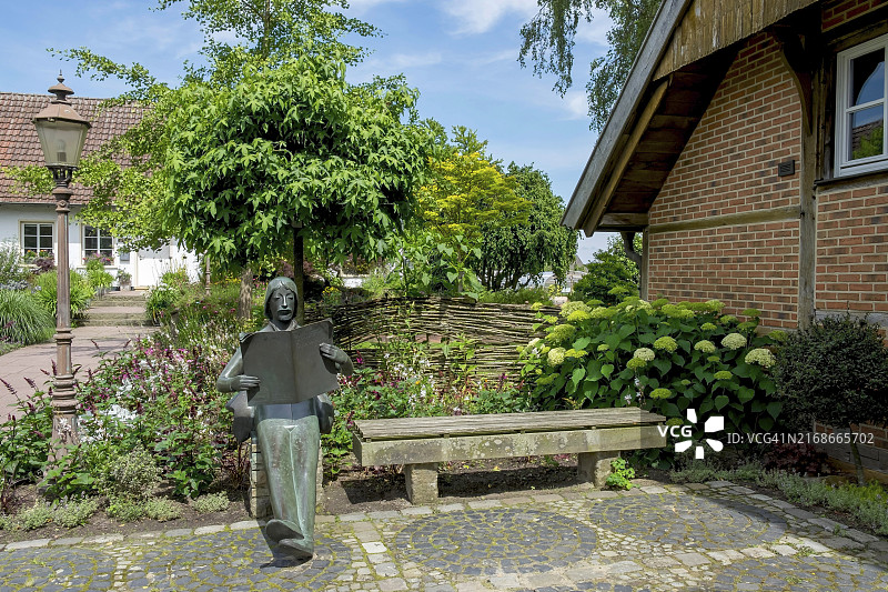 宁静花园中带书和长凳的青铜雕像。图片素材