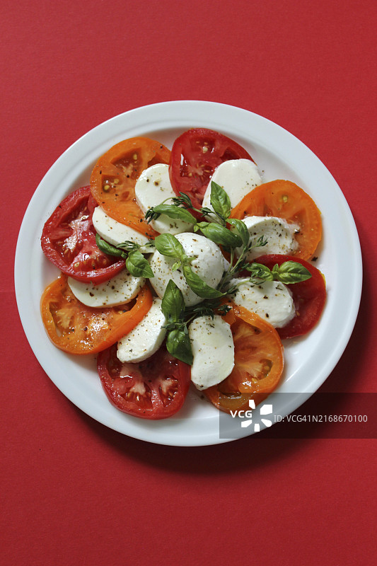 白盘红背景上的番茄马苏里拉奶酪卡普雷塞沙拉图片素材