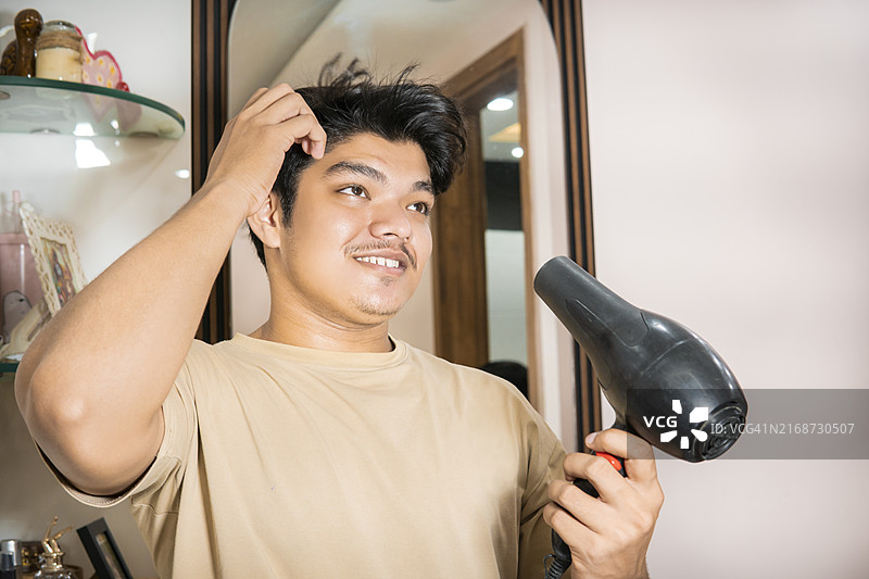 快乐的年轻女性在卧室里用吹风机吹干头发。图片素材