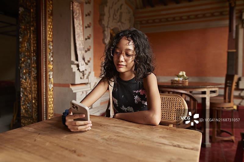 戴眼镜的女孩在寺庙的桌旁使用智能手机图片素材
