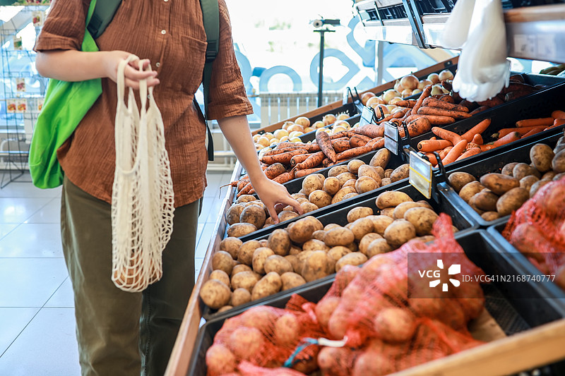 Z世代女孩购买有机土豆并装入可重复使用的棉网袋中，实现环保消费图片素材