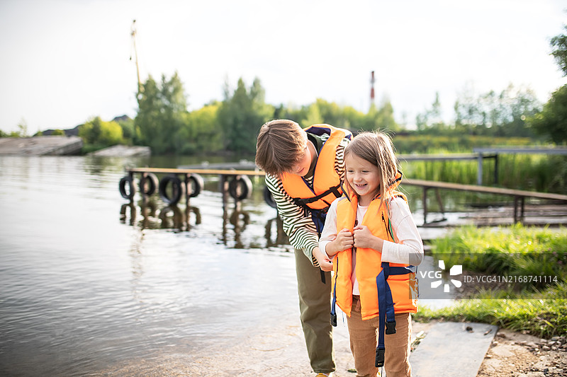 河边的兄妹：姐姐帮助妹妹穿救生衣，准备享受水上乐趣图片素材