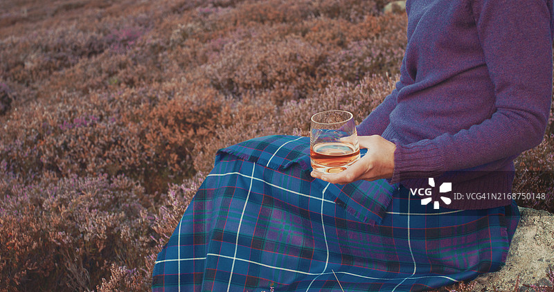 女人在苏格兰高地身穿传统基尔特裙倒一杯单一麦芽威士忌图片素材
