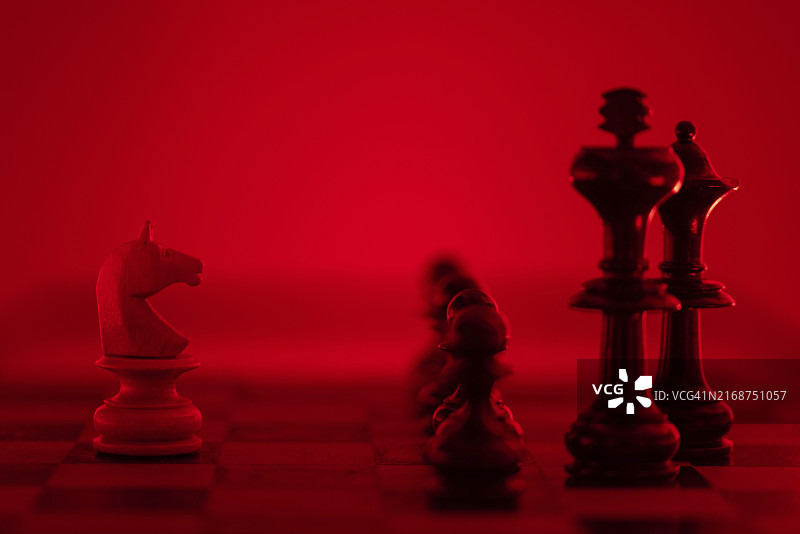 在红光中照亮的国际象棋棋子，焦点集中在前景中的白色骑士上图片素材