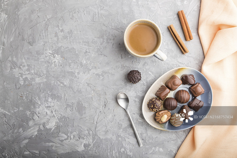 灰色混凝土背景和橙色纺织品上的不同巧克力糖果和一杯咖啡，俯视图，平铺，复制空间图片素材