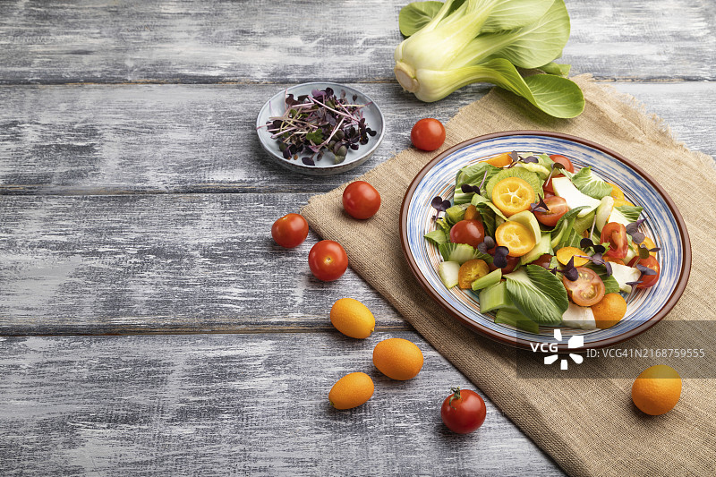 灰色木质背景和亚麻纺织品上的小白菜、猕猴桃、番茄、金橘、微绿芽苗素食沙拉。侧视图，留白图片素材