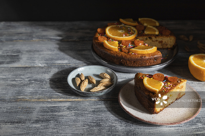 灰色木质背景上的橙色蛋糕，硬光，对比，低调。侧视图，留白图片素材
