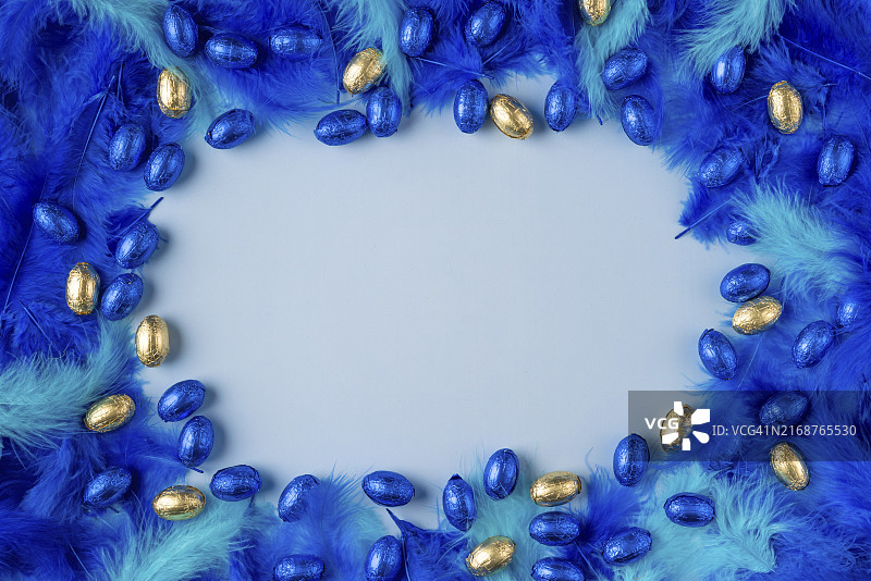 蓝绿色羽毛和蓝金巧克力蛋在浅蓝色背景上的框架图片素材