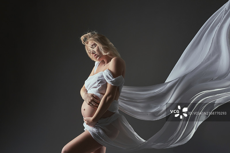 身穿白色连衣裙，抚摸腹部的孕妇侧视图图片素材