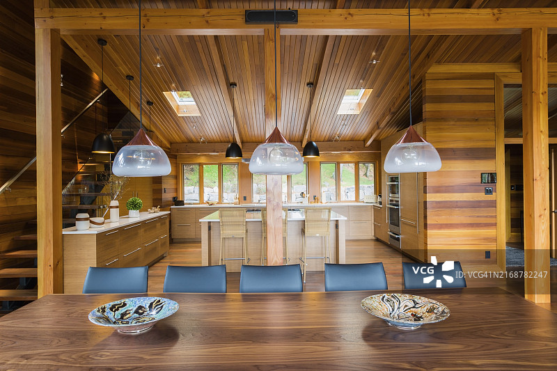 工业风铜制磨砂玻璃吊灯，木制餐桌配黑色皮椅，背景是带竹木岛台和橱柜的厨房图片素材