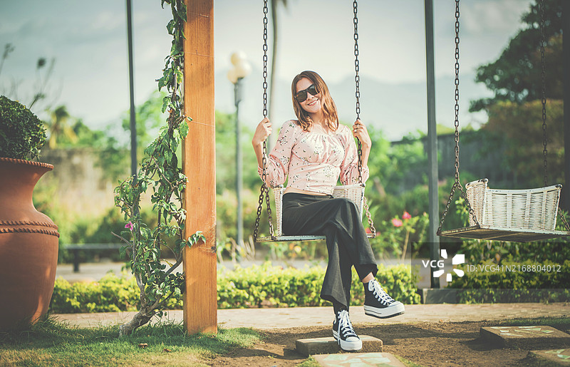 在自然公园的秋千上快乐摇摆的年轻女人图片素材