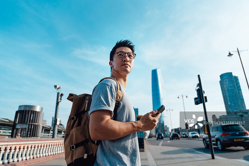 在城市街道上使用智能手机的年轻亚洲男人。图片素材
