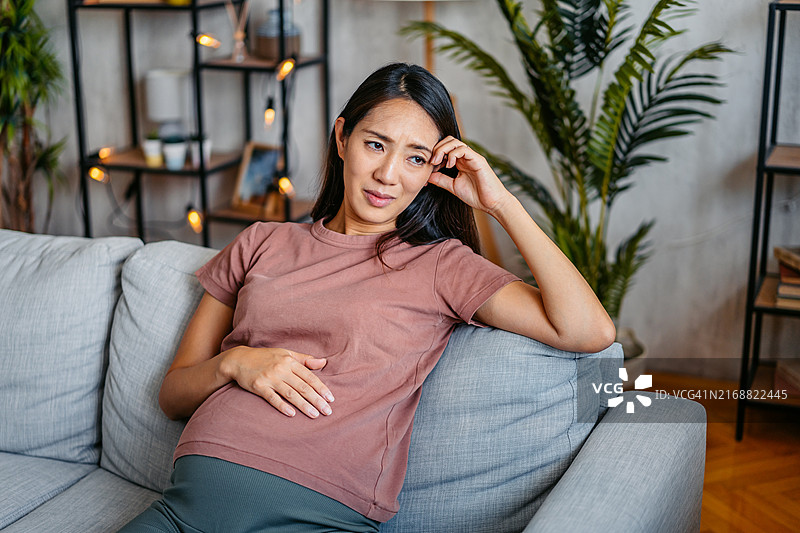 坐在家中沙发上的悲伤中年怀孕亚洲妇女图片素材