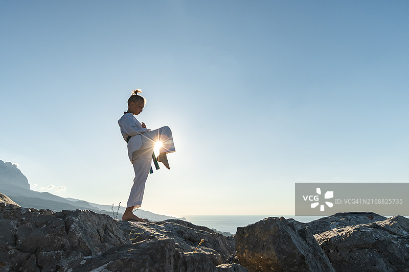 武术练习——专注的年轻男孩在日出时在岩石地形上训练跆拳道图片素材