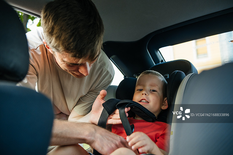 儿童乘车安全：父亲用安全带将儿子固定在汽车座椅上图片素材