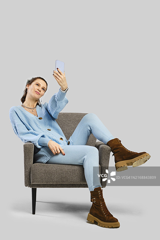 一位身穿蓝色针织套装的女士舒适地坐在椅子上使用智能手机图片素材