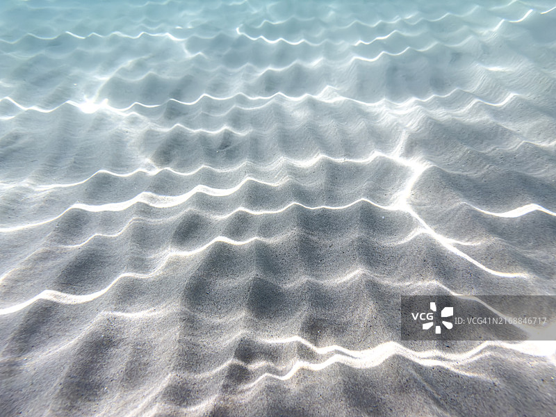 清澈海水中沙底上的波浪图案和光线反射图片素材