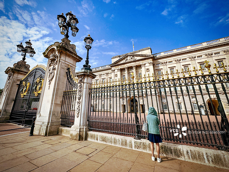 一位女性站在白金汉宫的大门外，透过栅栏欣赏宫殿。图片素材
