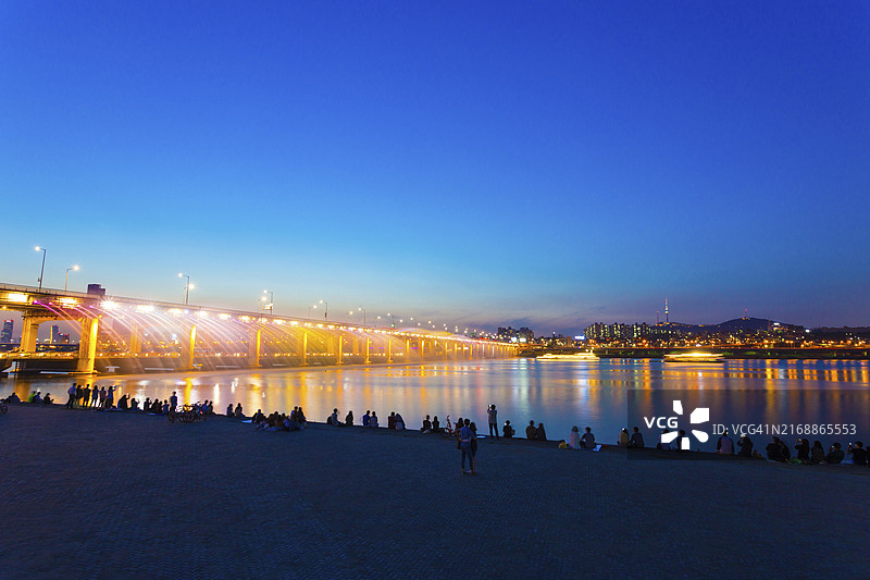 人们在晴朗的夜晚，在韩国首尔江南的汉江上的盘浦大桥观看月光彩虹喷泉和彩色灯光秀。图片素材